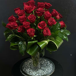 Red roses arranged in a clear vase with glossy leaves