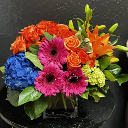Colorful bouquet with roses, gerbera daisies, hydrangea, and lilies in a glass vase