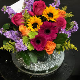 Bright mixed bouquet with roses, gerbera daisies, sunflowers, and purple blooms in a vase