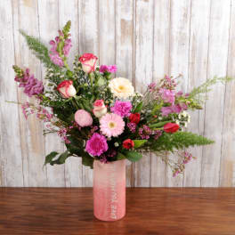Tall mixed bouquet of pink, cream, and red flowers in a pink vase labeled 'Love You Mean It'.