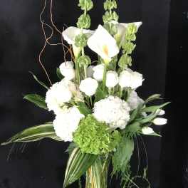 White calla lilies and hydrangeas in a glass vase with green accents