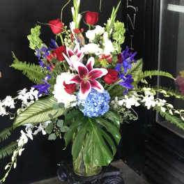 Tall mixed bouquet with red roses, lilies, and blue hydrangea in a glass vase