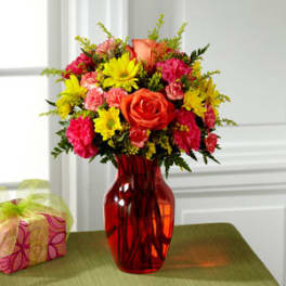 Mixed bouquet of roses, daisies, and carnations in a red glass vase