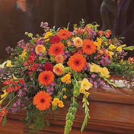 Bright mixed casket spray with orange gerberas and yellow roses on a wooden casket