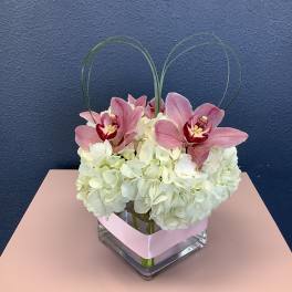 Pink orchids and white hydrangeas in a square glass vase with looped grass