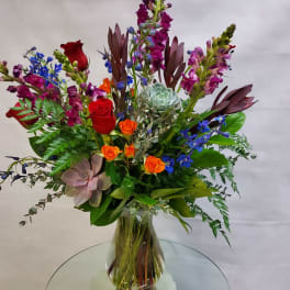 Mixed bouquet in a glass vase with red and orange roses, blue flowers, and a succulent