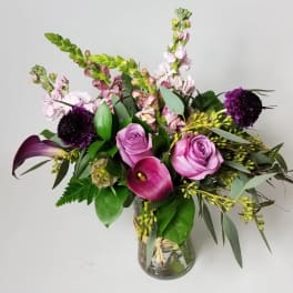 Purple roses and calla lilies in a glass vase with mixed greenery