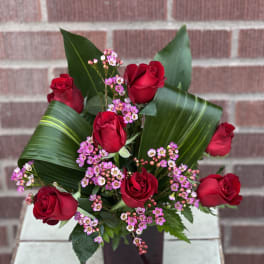 Red roses with pink waxflower in a dark vase