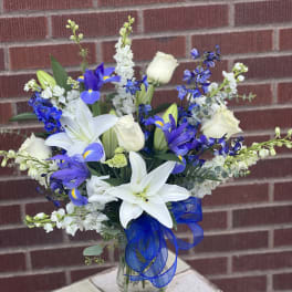White lilies and blue-purple flowers in a glass vase with a blue ribbon