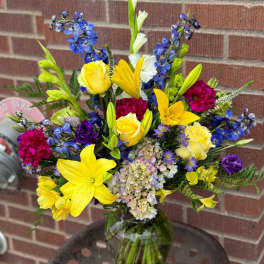 Mixed bouquet in a glass vase with yellow lilies, roses, and blue flowers