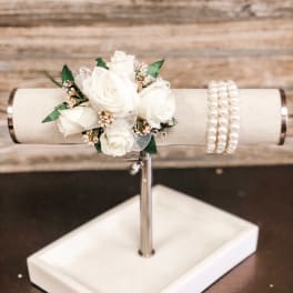 White rose corsage on a display stand with pearl bracelets