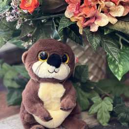 Plush otter beside a floral arrangement with pink hydrangeas and orange blooms