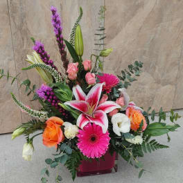 Mixed bouquet with pink lilies, roses, and gerbera daisies in a square vase