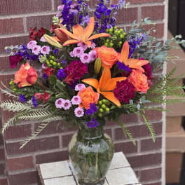 Bright mixed bouquet in a glass vase with orange lilies and roses