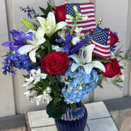 Red roses and white lilies in a blue vase with small American flags