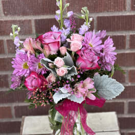 Pink and lavender bouquet in a glass vase with a bright ribbon