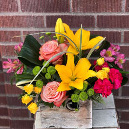 Colorful bouquet with yellow lilies, pink roses, and bright pink carnations in a wooden box