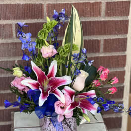Pink and white lilies with blue flowers in a square vase