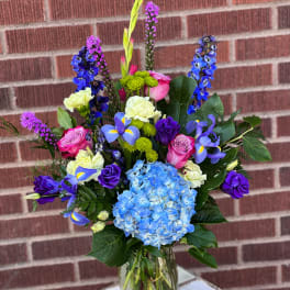 Mixed bouquet of blue hydrangea, pink roses, and purple flowers in a glass vase