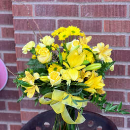 Yellow mixed bouquet in a clear glass vase with a ribbon bow