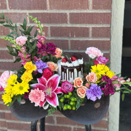 Colorful floral arrangement with a small cake centerpiece in a black container