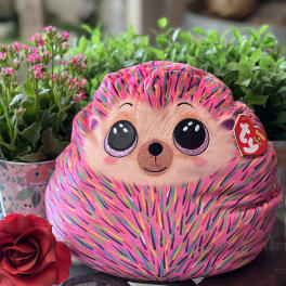 Pink plush hedgehog toy with a red rose and potted flowers behind it