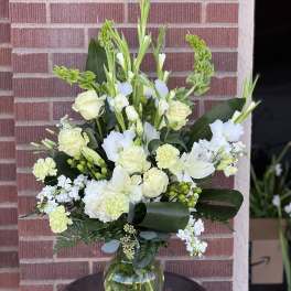 White floral arrangement in a clear glass vase with tall greenery accents