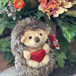 Plush hedgehog holding a red heart in front of orange flowers