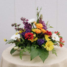Mixed bouquet with roses, daisies, and purple blooms in a low white container