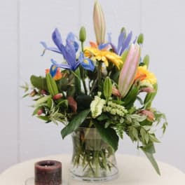 Mixed bouquet in a clear glass vase with a candle beside it
