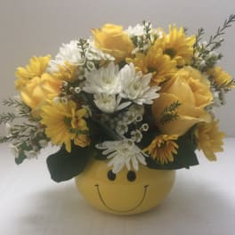 Yellow and white flower arrangement in a smiley-face container