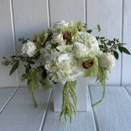 White floral arrangement with roses, hydrangeas, and green orchids in a white vase