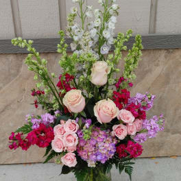 Tall mixed bouquet of pink roses, purple blooms, and white flowers in a glass vase