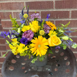 Yellow and purple mixed flower arrangement in a gray vase
