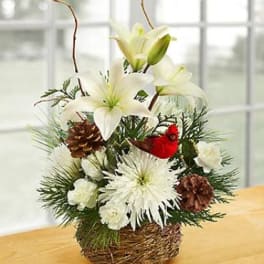 White lilies and chrysanthemums in a woven basket with pinecones and a red cardinal ornament