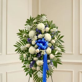Standing floral wreath with white and blue flowers and a blue ribbon