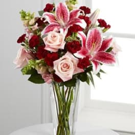 Bouquet of pink lilies, roses, and red carnations in a clear glass vase