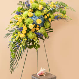 Large floral spray with yellow roses, blue flowers, and green blooms on a stand
