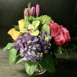 Mixed bouquet with roses, hydrangea, tulips, and orchid in a glass vase