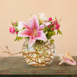 Pink lily and small pink roses in a round glass vase