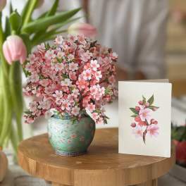 Pink cherry blossom arrangement in a green patterned vase beside a matching card