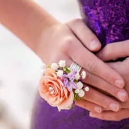 Hand wearing a peach rose corsage with small white and purple flowers