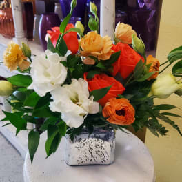 Mixed bouquet of orange, white, and yellow flowers in a square vase