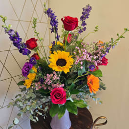 Tall mixed bouquet with roses, sunflowers, and gerbera daisies in a white vase