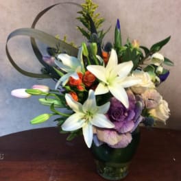 Mixed bouquet with white lilies and purple blooms in a glass vase