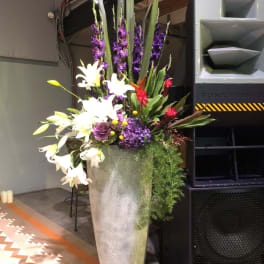 Tall floral arrangement in a silver vase with white lilies and purple blooms