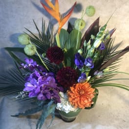 Tropical floral arrangement with purple orchids and orange blooms in a vase