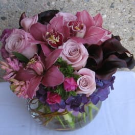 Pink and purple bouquet with roses, orchids, and calla lilies in a glass vase