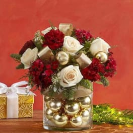 Red and white roses arranged in a clear vase filled with gold ornaments