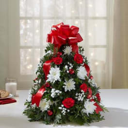 Cone-shaped holiday floral arrangement with red ribbon and white flowers